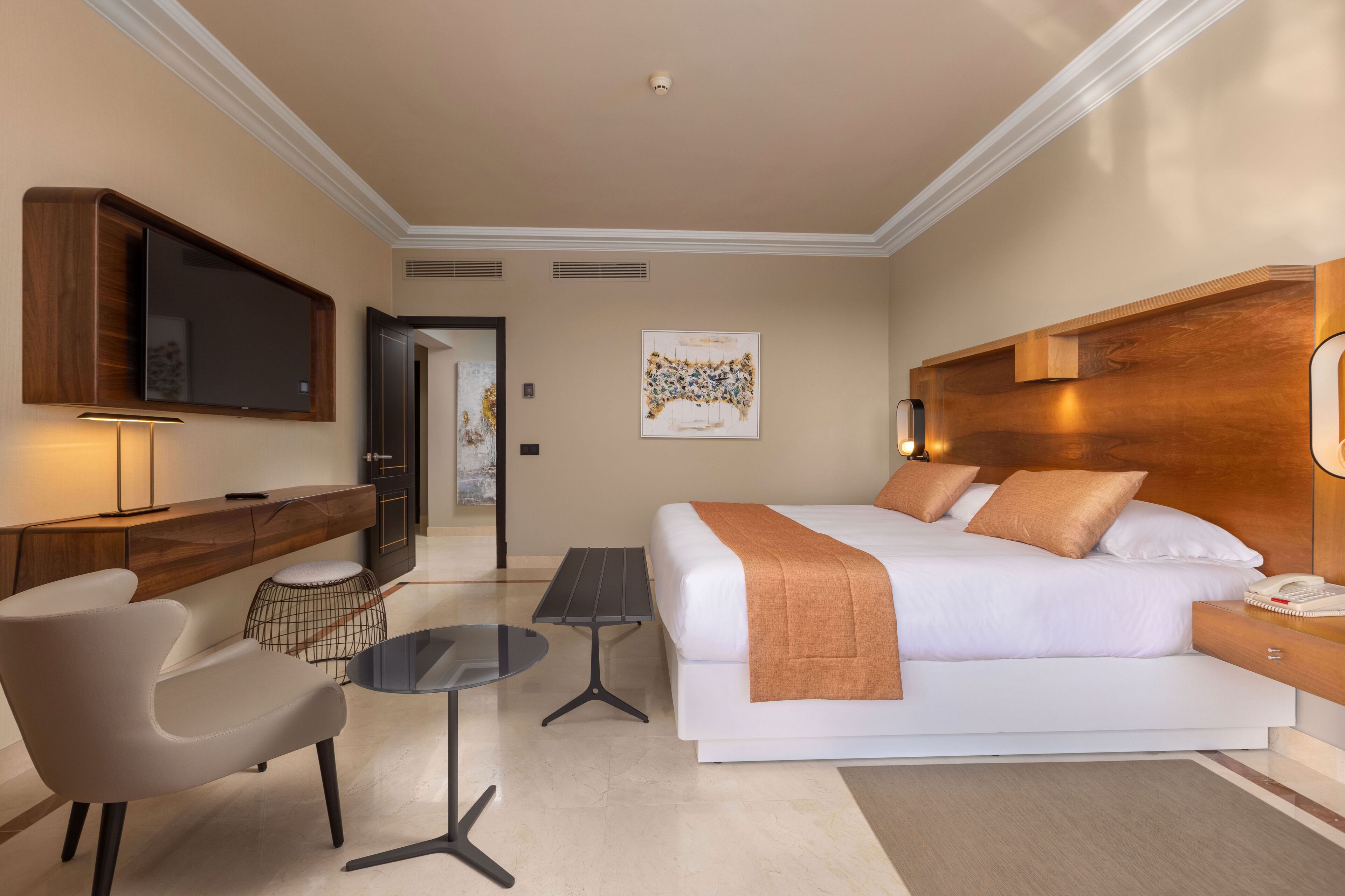 A modern hotel room with a large bed, a desk, a chair, a TV, and a small table.