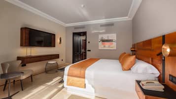 Una habitación de hotel con una cama grande, un escritorio con lámpara, un televisor montado en la pared y un cuadro colgado.