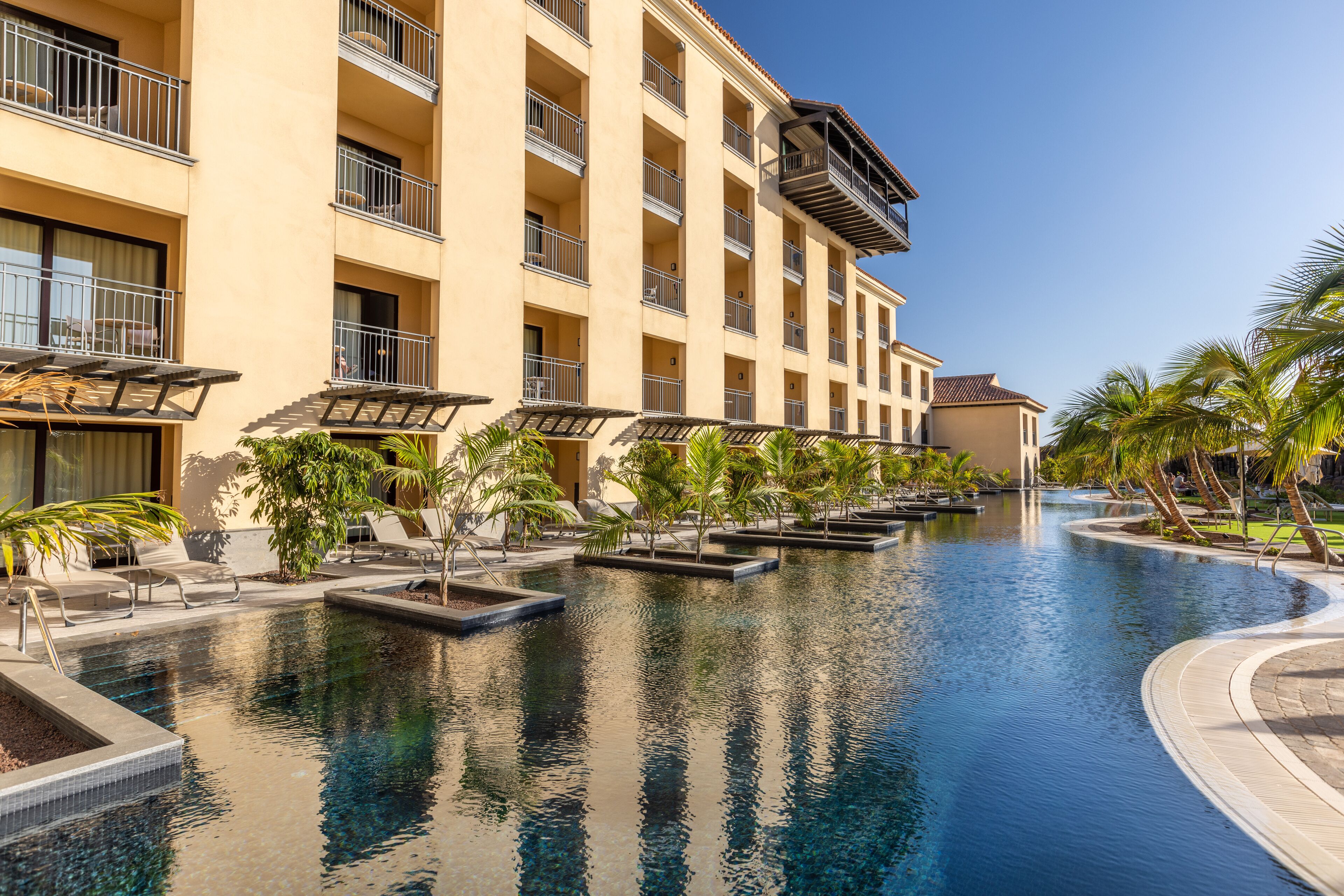 A hotel with a swimming pool, multiple balconies, and palm trees.