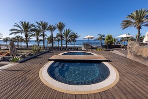Zona de piscina con hidromasaje, sillas de descanso y sombrillas, con vista al océano.
