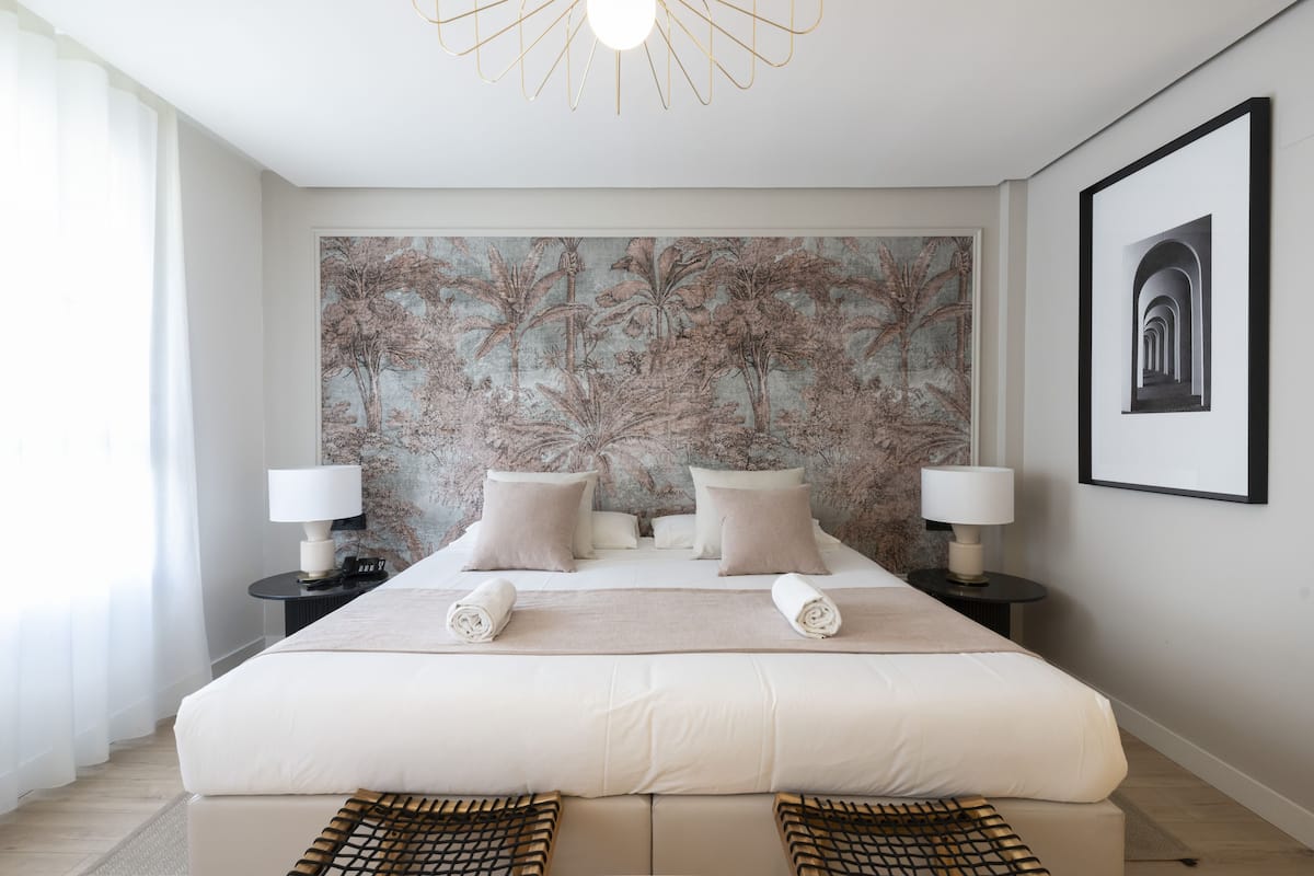A modern hotel room with a large bed, two bedside tables with lamps, a large floral mural on the wall, and a framed picture on the wall.