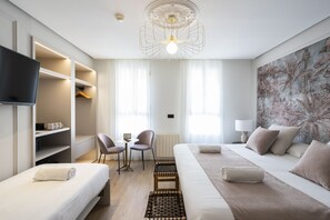 A modern hotel room with a bed, a TV, a desk with chairs, and a large window with curtains. - YOU & CO. J. Botánico Boutique Hotel (Valencia)