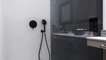 Un baño moderno con ducha de vidrio, pared de azulejos blancos y un área de lavamanos visible con espejo y encimera.