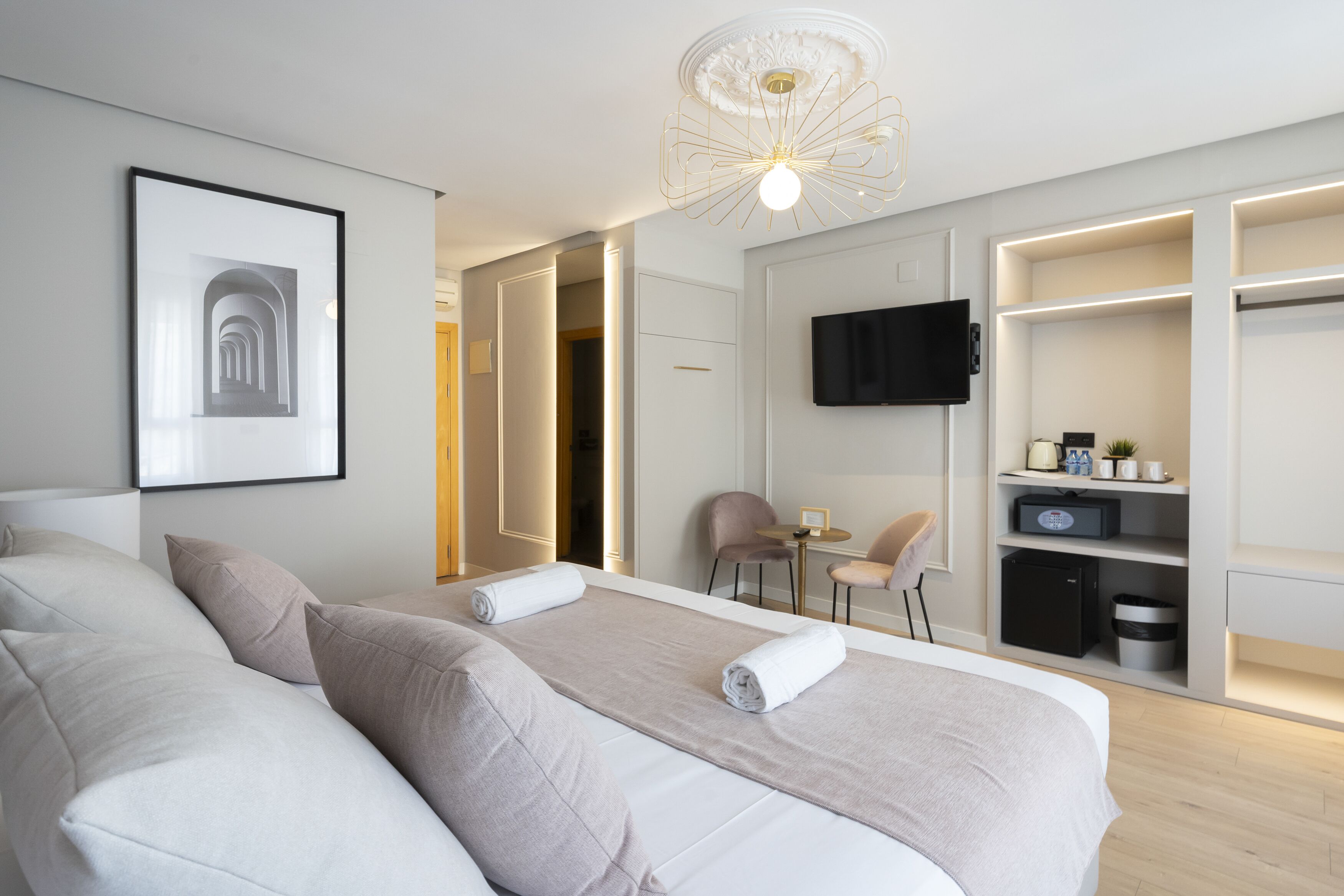 Ein modernes Hotelzimmer mit einem großen Bett, einem Schreibtisch, einem Sessel, einem Fernseher und integrierten Stauraum.