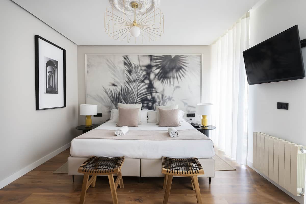 A modern bedroom with a large bed, two bedside tables, a mounted TV, and a large abstract painting on the wall.