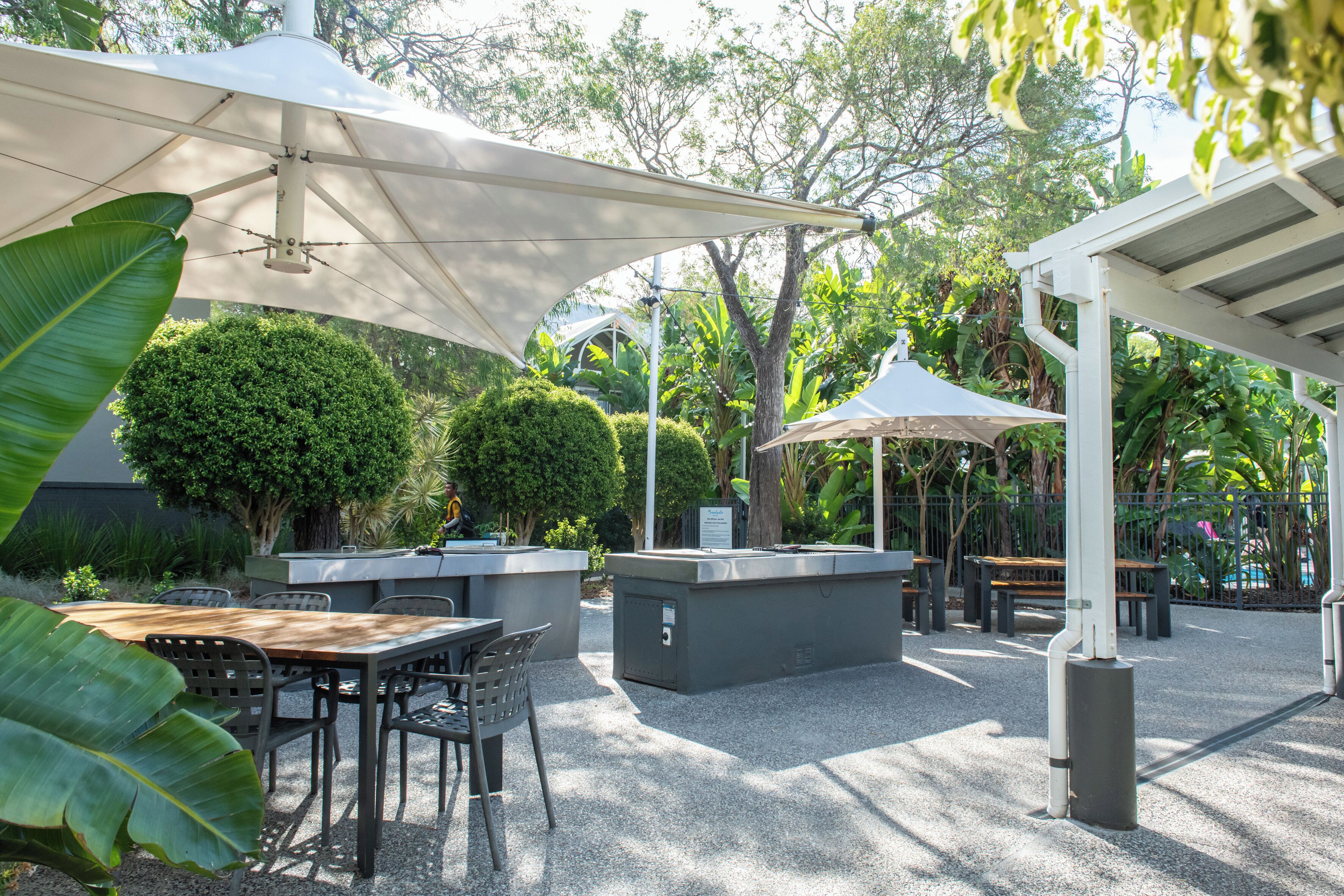 An outdoor patio area with a wooden table and chairs, a barbecue grill, and umbrellas providing shade.