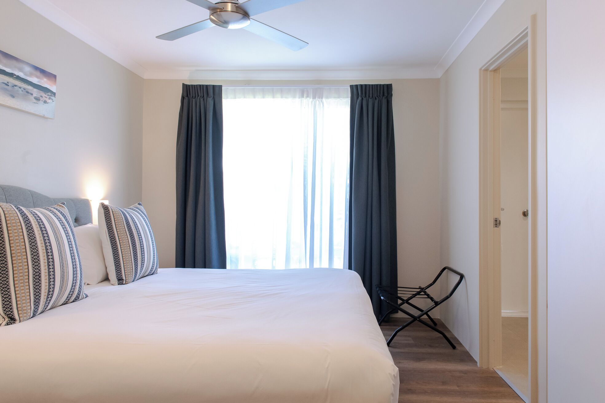 Een hotelkamer met een bed, een plafondventilator, een raam met gordijnen, een stoel en een deur.