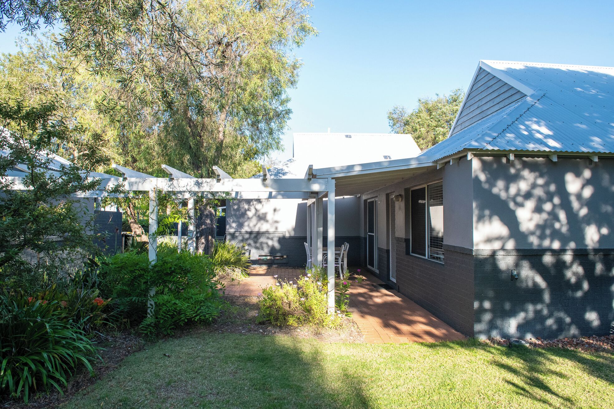 A residential property with a covered patio, a brick pathway, and a garden area with various plants and flowers.