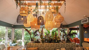 Een gezellig restaurantinterieur met hangende rieten lampen, een gestreept bankje en potplanten.
