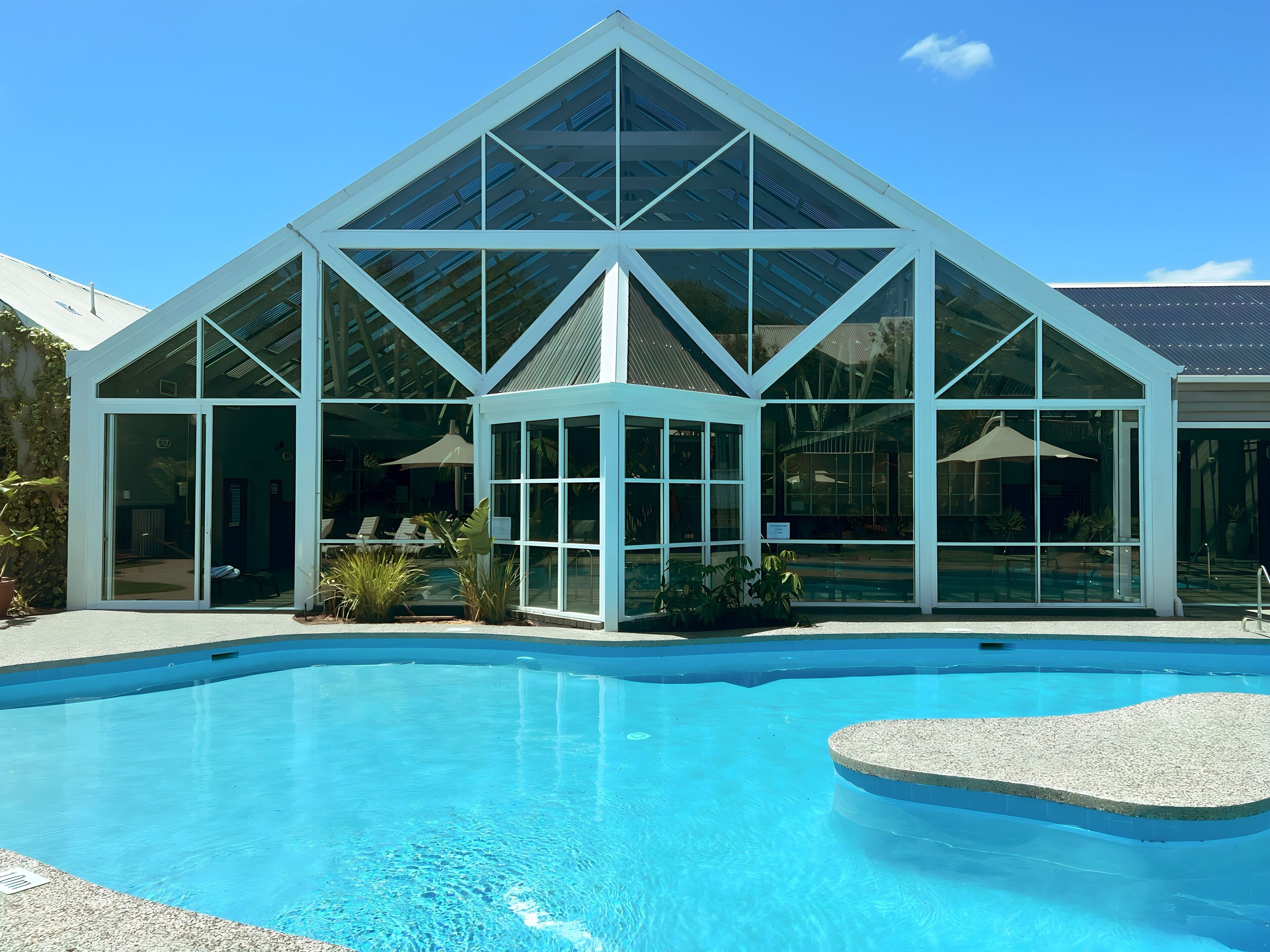 A modern building with a glass facade and a pool in front.