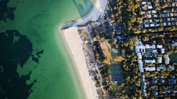 Luchtbeeld van een kustgebied met strand, woongebouwen en een tennisbaan.
