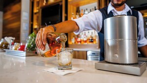 Een barman giet een drankje in een glas met ijs.