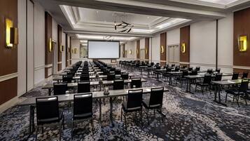 A conference room with rows of tables and chairs, a large screen, and a carpeted floor.