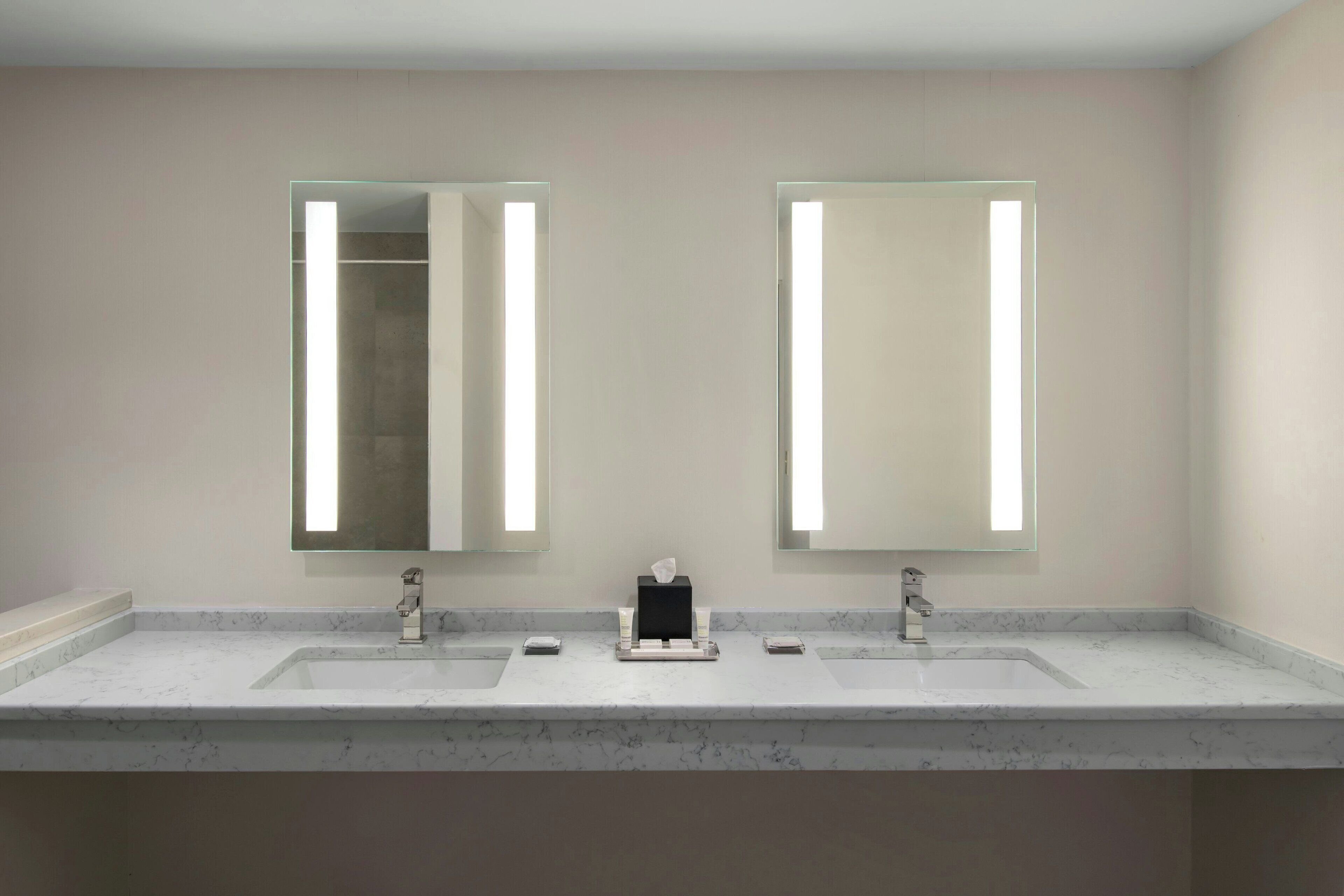 Un baño con encimera de mármol, dos lavamanos y un espejo con iluminación integrada.