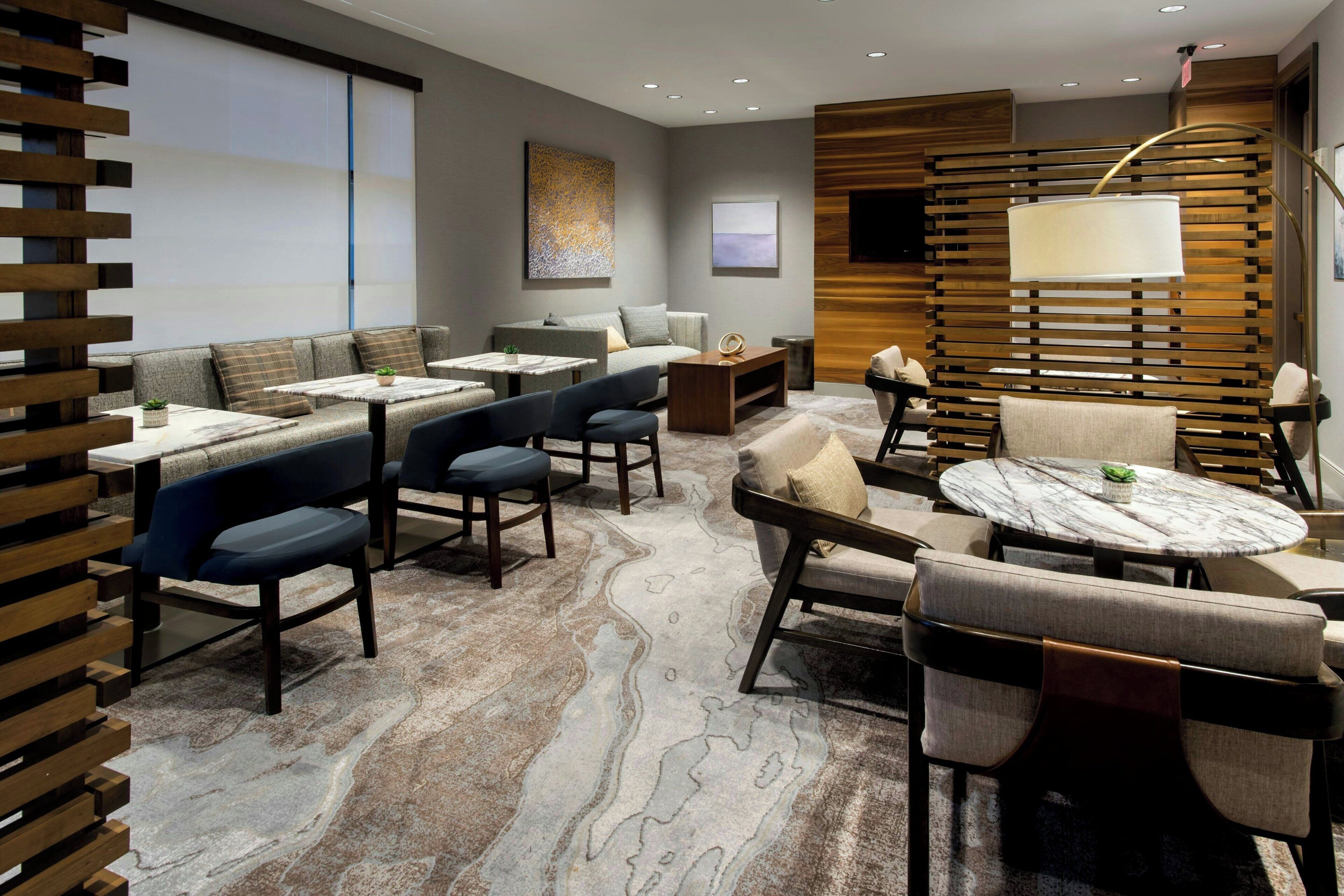 A modern hotel lobby with seating areas, a marble-patterned carpet, and a large wooden partition.