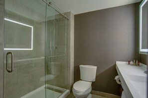 Un baño con ducha de vidrio, inodoro y lavamanos con artículos de aseo.