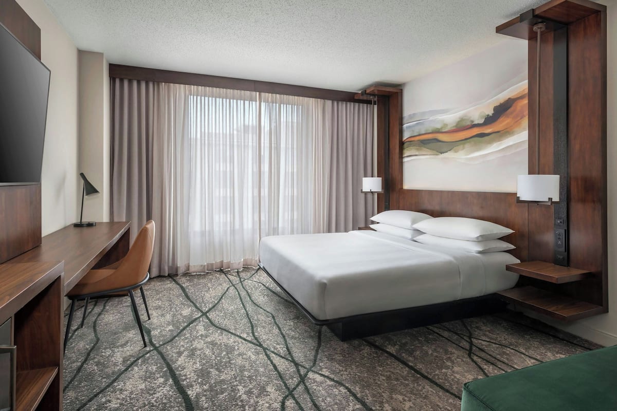 A hotel room with a bed, a desk, a chair, and a large window with curtains.