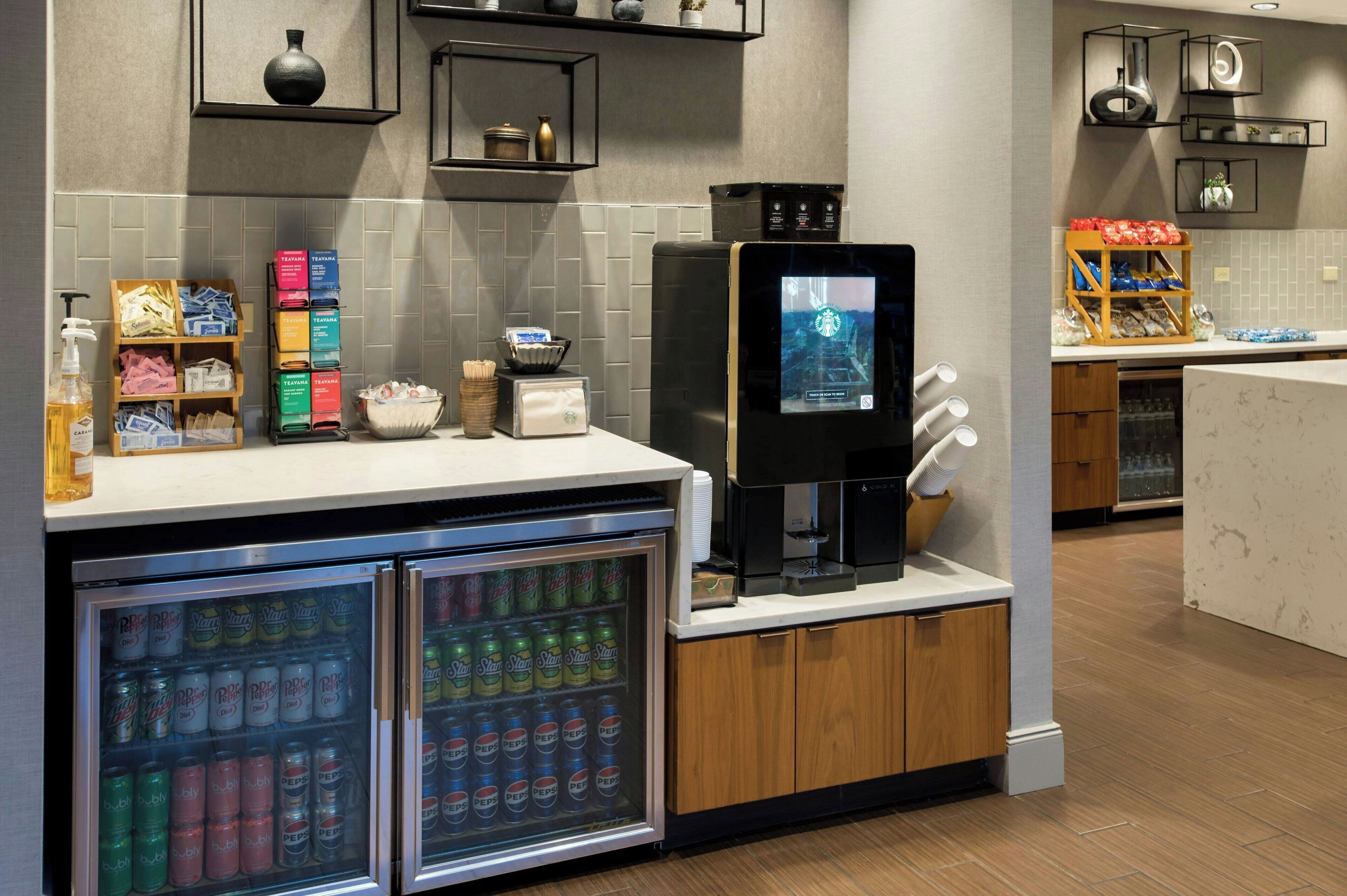 Ein moderner Küchenbereich mit Kaffeemaschine, Getränkeautomaten und Kühlschränken, gefüllt mit Getränken.