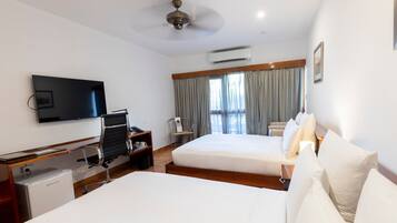 A hotel room with two beds, a desk, a chair, a television, and an air conditioning unit.