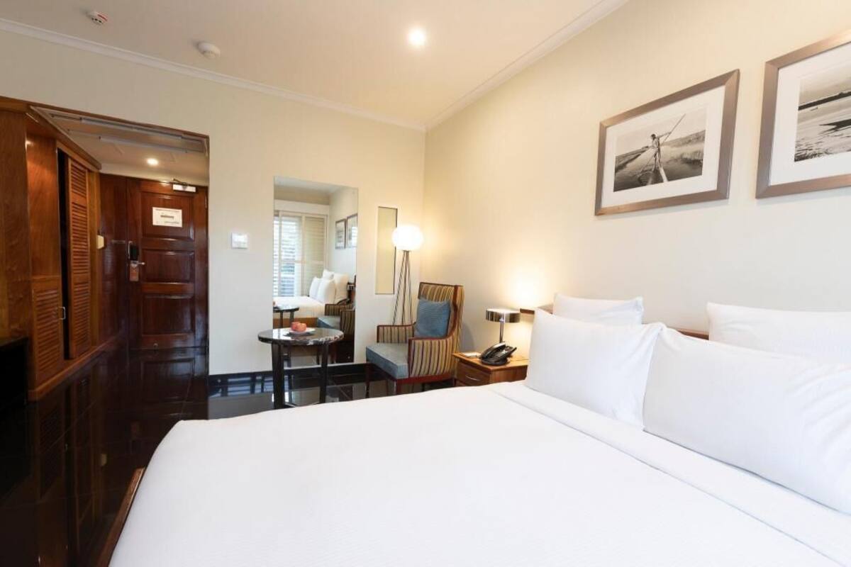 A hotel room with a large bed, a desk, a chair, a lamp, and two framed pictures on the wall.
