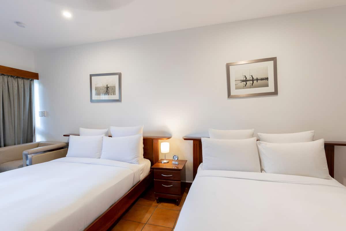 A hotel room with two beds, a nightstand with a lamp, and two framed pictures on the wall.