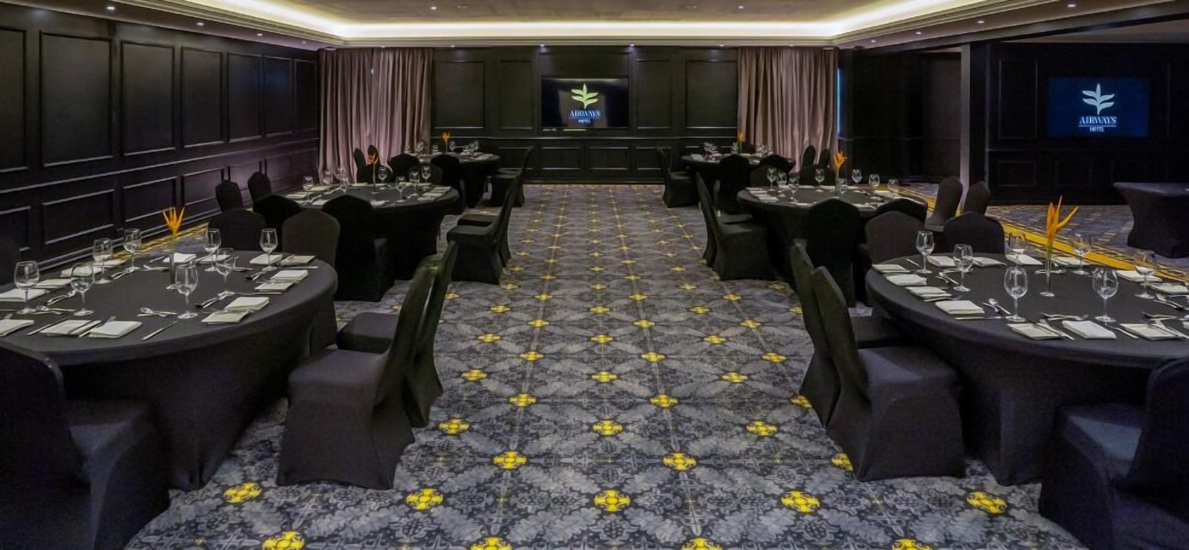 Un salón de conferencias con mesas redondas, sillas negras y una alfombra estampada.