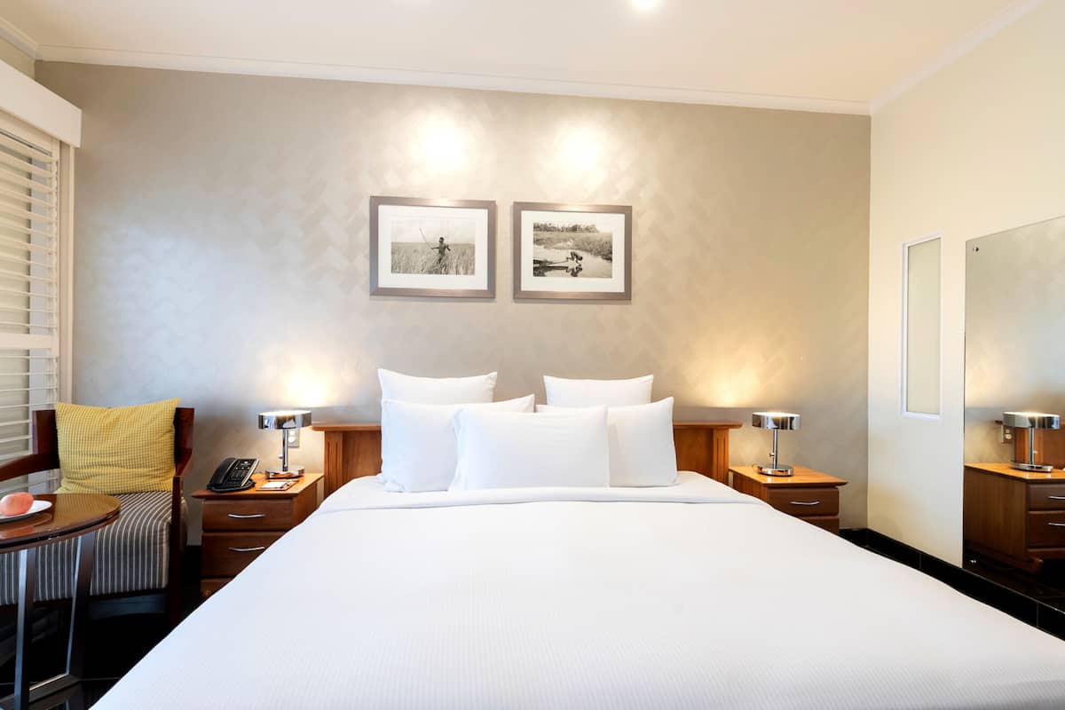 A hotel room with a large bed, two bedside tables with lamps, a chair with a yellow cushion, and two framed pictures on the wall.