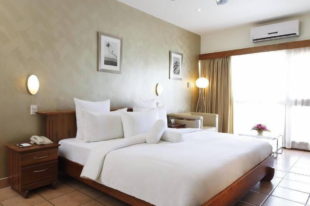 A hotel room with a large bed, bedside tables, a desk, and a window with curtains.