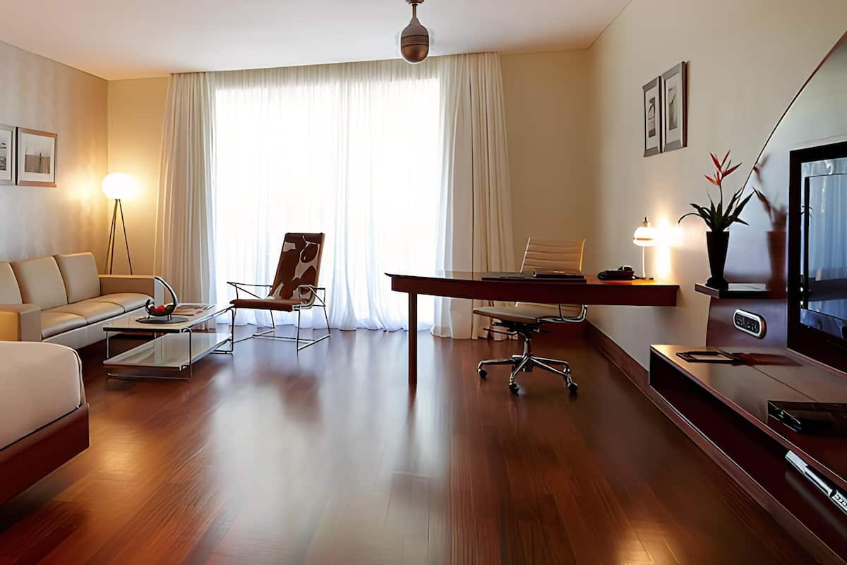 A hotel room with a bed, a sofa, a desk, a chair, a TV, and a lamp.