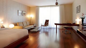 A hotel room with a bed, a sofa, a desk, a chair, a TV, and a lamp.