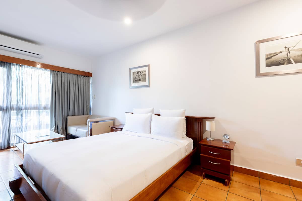 A hotel room with a large bed, a desk, a chair, a nightstand, and a framed picture on the wall.