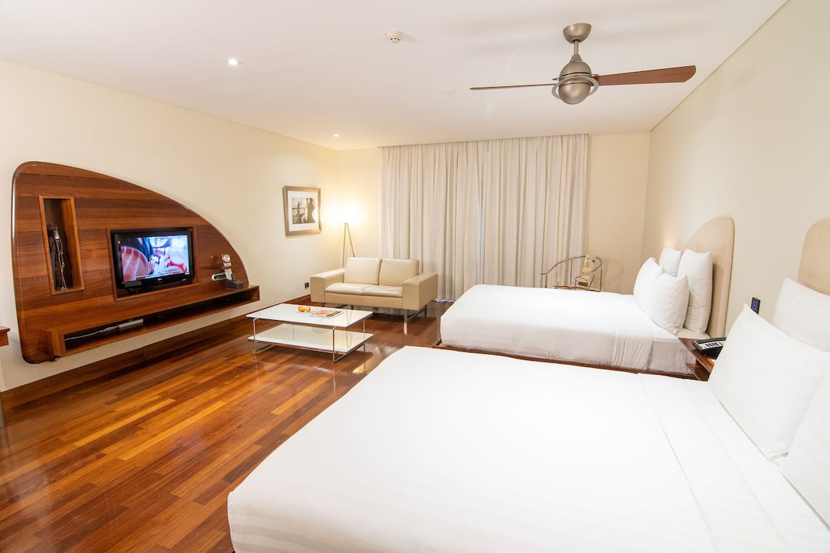 A hotel room with a wooden entertainment unit, a flat-screen TV, a sofa, a bed, and a ceiling fan.