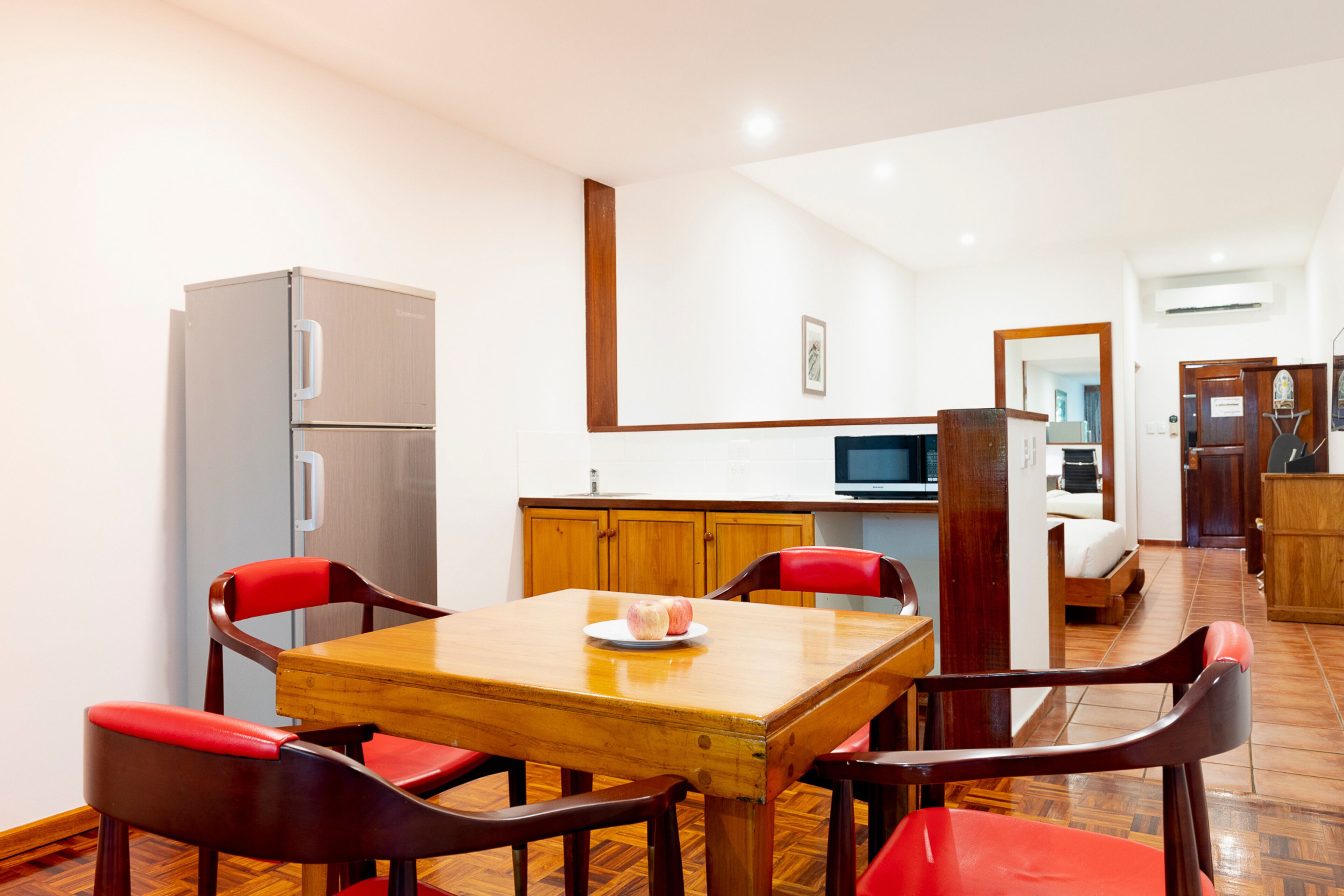 A dining area with a wooden table and red chairs, a refrigerator, wooden cabinets, and a television.