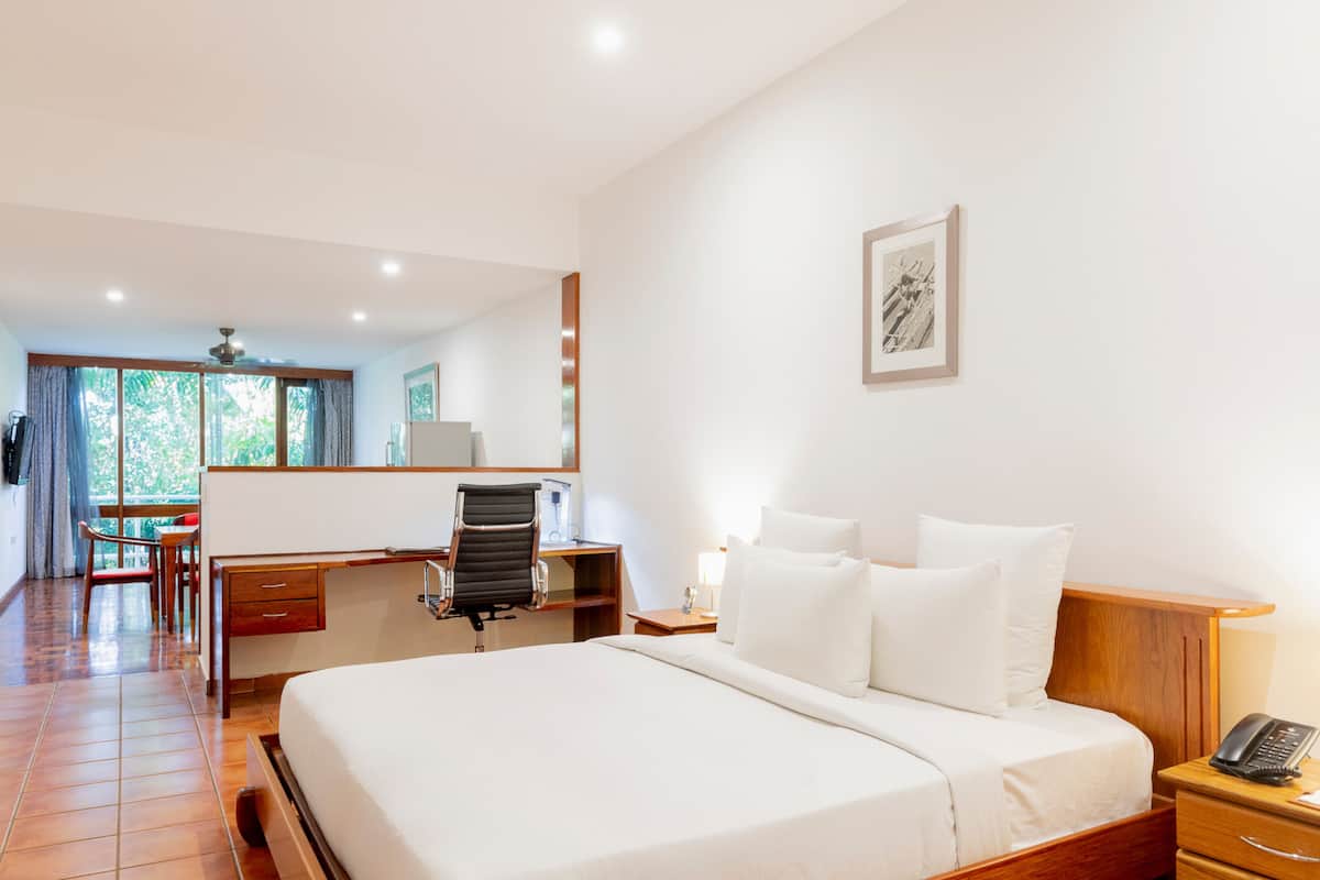 A hotel room with a large bed, a desk with a chair, a small table, and a nightstand with a phone.