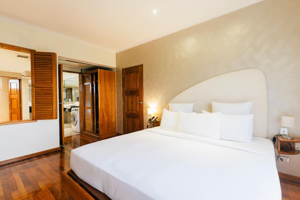 A hotel room with a large bed, wooden flooring, a wardrobe, and a mirror.