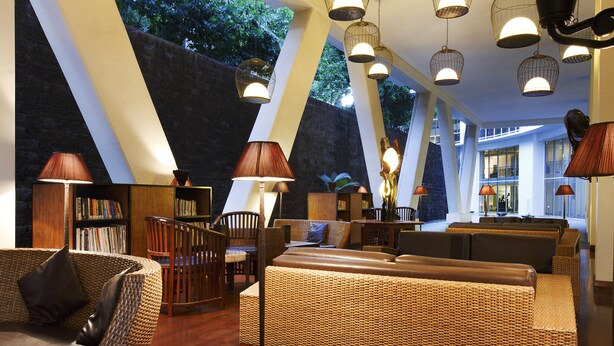 A spacious lounge area with a large wicker sofa, multiple seating options, and a bookshelf. - Airways Hotel (Port Moresby)