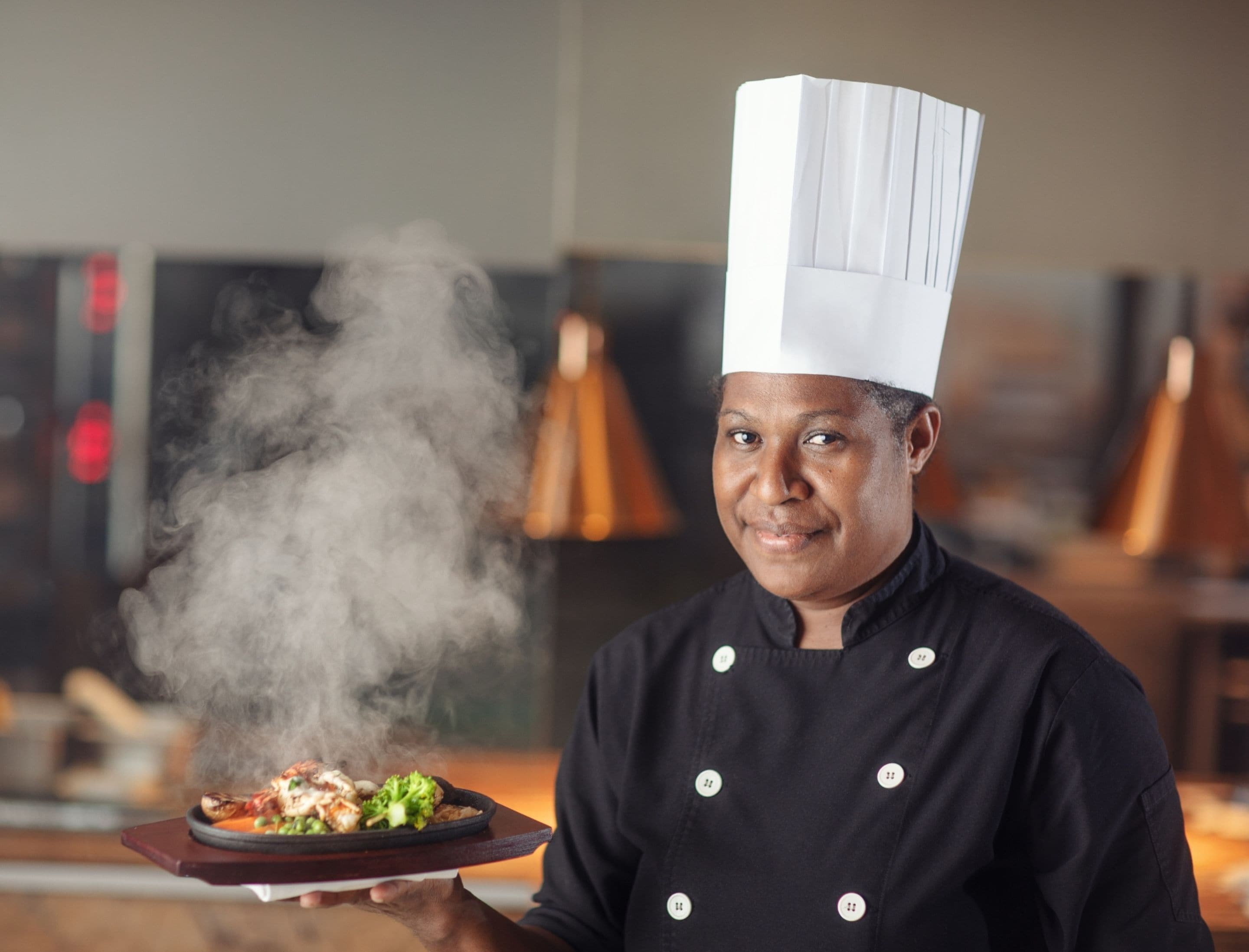 A chef holding a plate of food with steam rising from it.