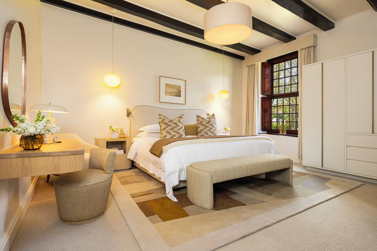 A modern bedroom with a large bed, bedside tables, a bench, and a window with curtains.
