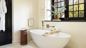 Ein modernes Badezimmer mit freistehender Badewanne, einem Holznachttisch, einer Topfpflanze und einem gerahmten Bild an der Wand.