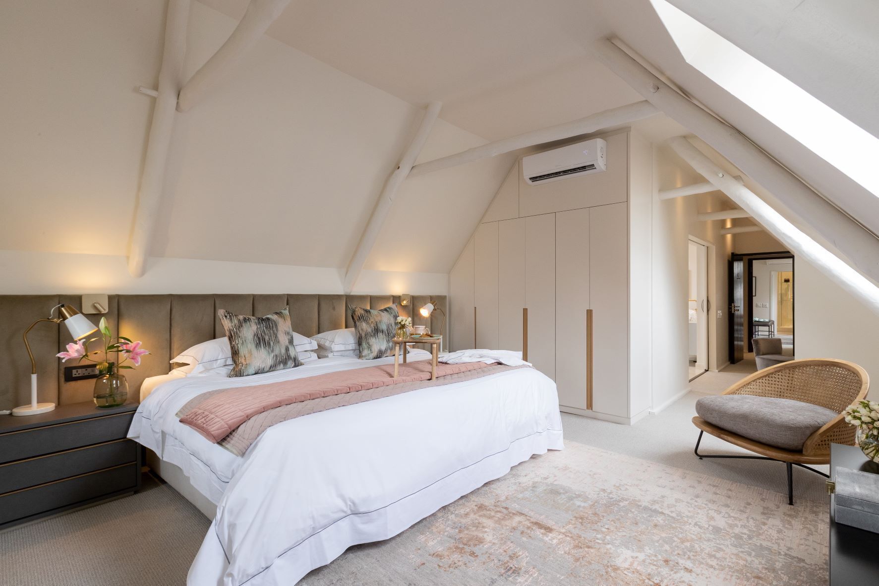 A bedroom with a large bed, bedside tables, a chair, and an air conditioning unit.