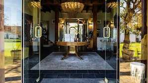 Vestíbulo con paredes de vidrio, una mesa de madera, un candelabro y vistas al exterior.