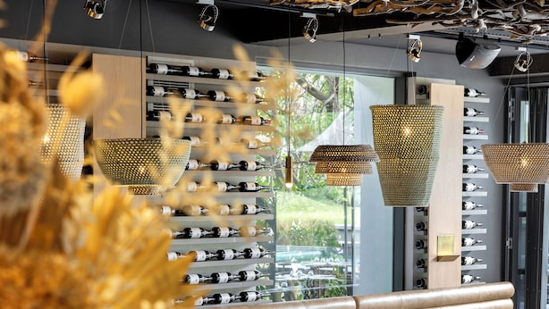 Interior de restaurante con botelleros, asientos y luces colgantes.