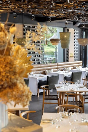 Interior de restaurante con botelleros, asientos y luces colgantes.