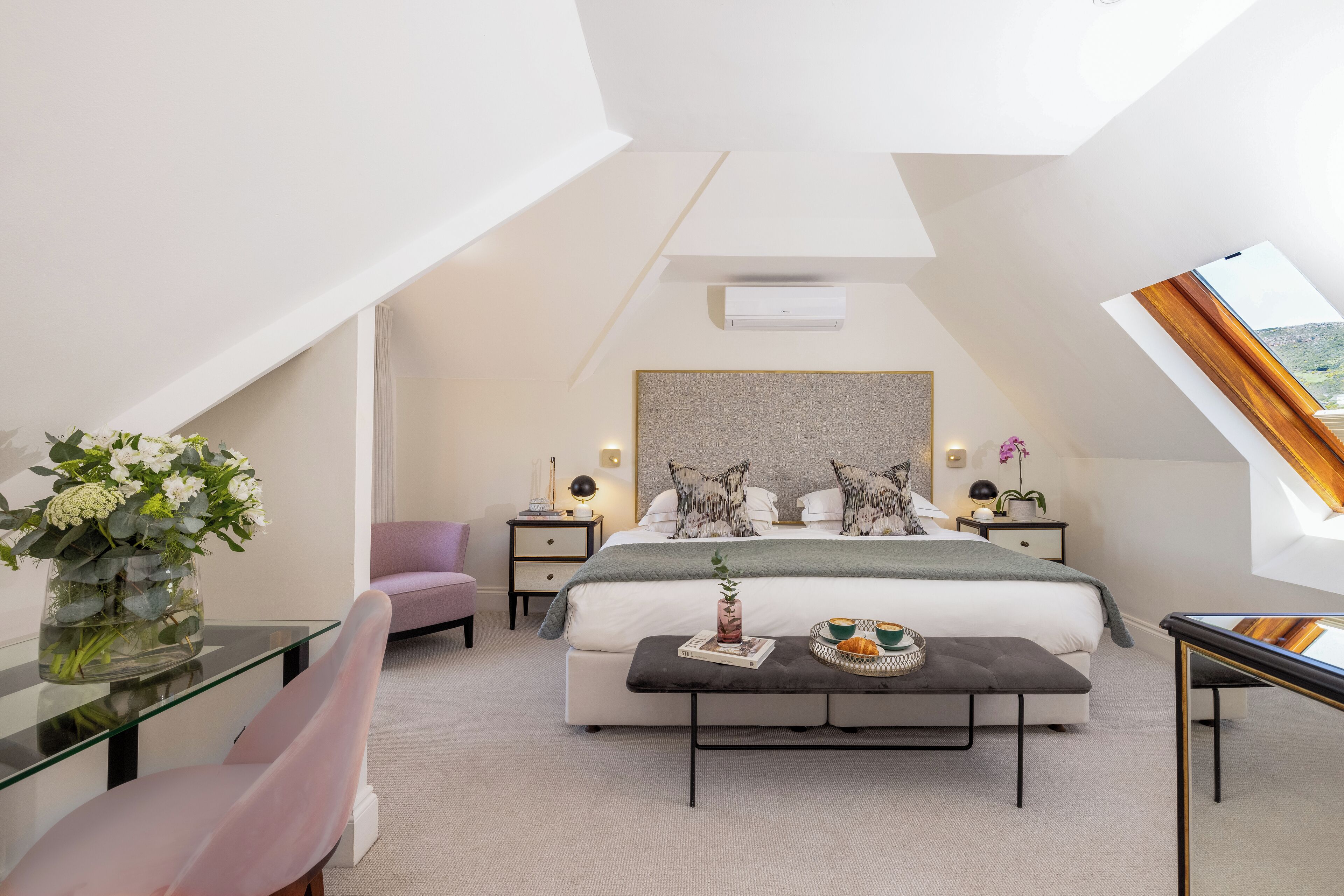 Un dormitorio moderno con una cama grande, mesitas de noche, una mesa de centro de vidrio y vistas al exterior.