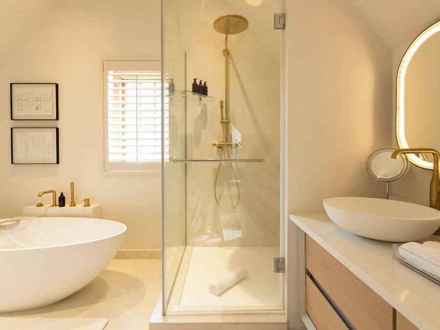 Une salle de bain moderne dotée d’une grande baignoire sur pied, d’une douche à parois de verre et de deux vasques avec des robinets dorés.