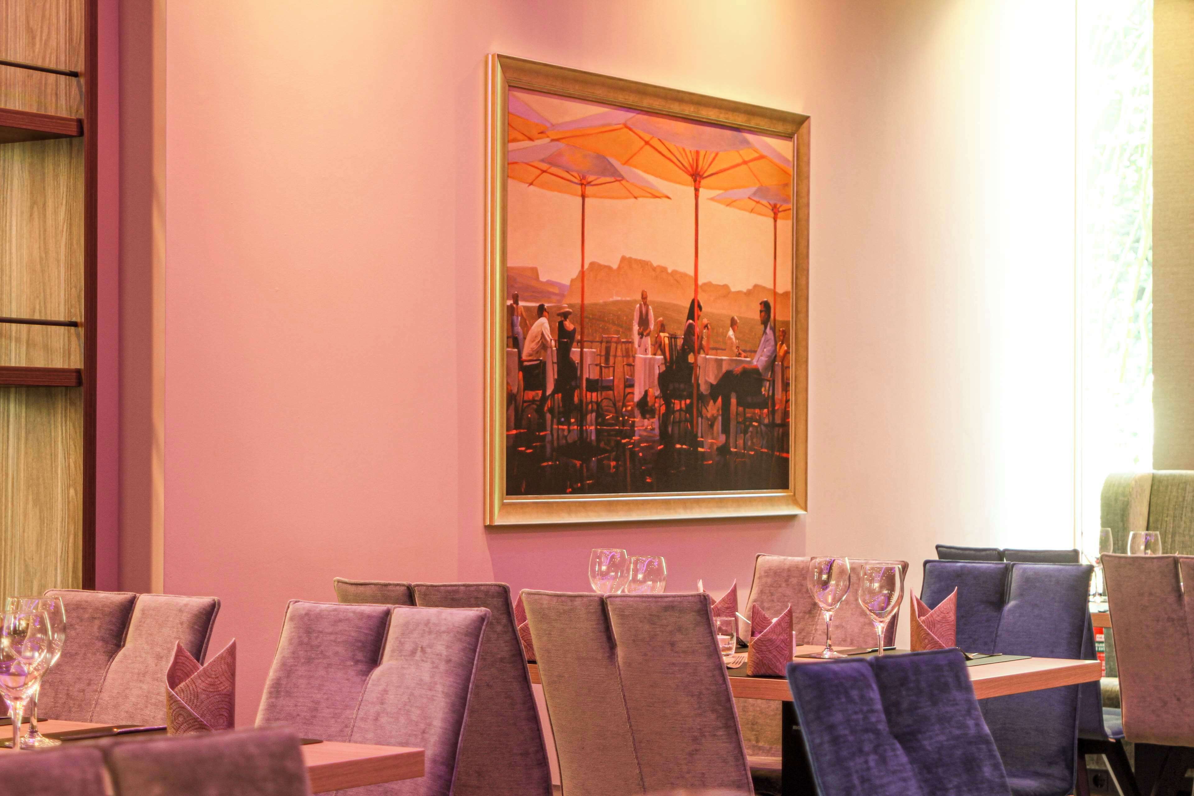 A restaurant with purple upholstered chairs, tables with wine glasses, and a large framed painting on the wall.