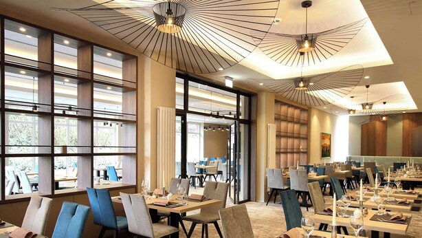 Un comedor moderno con varias mesas y sillas, ventanas amplias y lámparas de diseño contemporáneo.