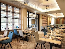 Un comedor moderno con varias mesas y sillas, ventanas amplias y lámparas de diseño contemporáneo.