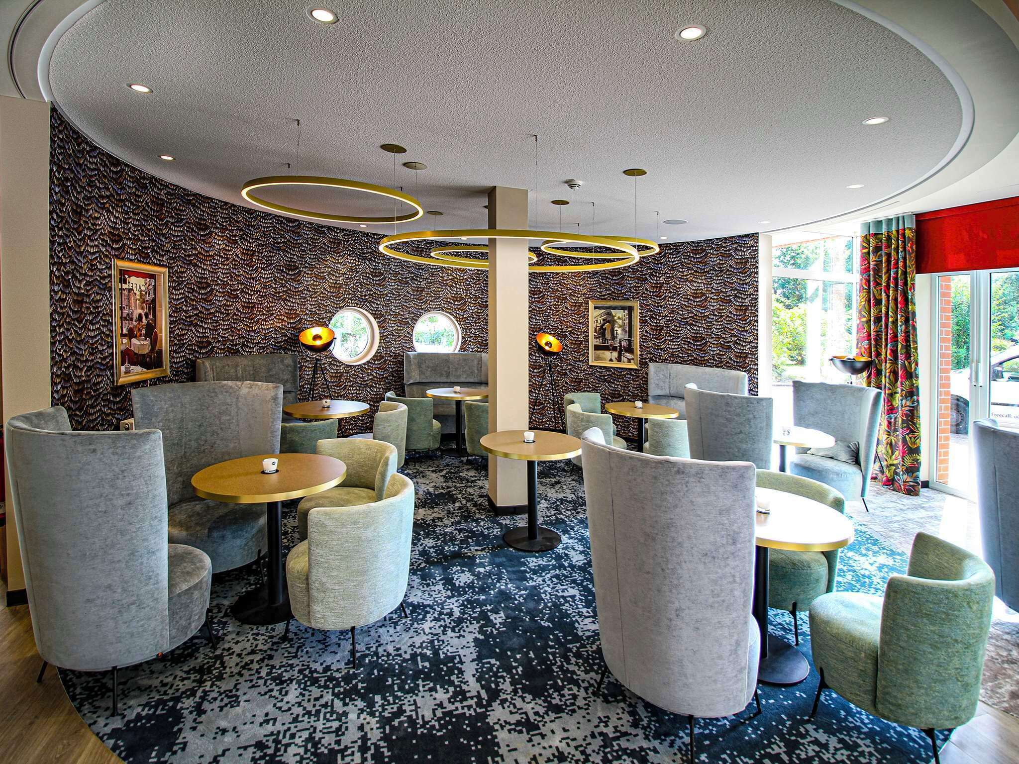 A modern lounge area with round tables and comfortable seating, featuring a patterned wall and ceiling design.