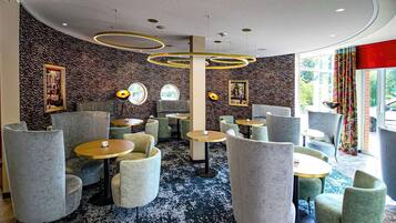 A modern lounge area with round tables and comfortable seating, featuring a patterned wall and ceiling design.